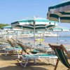 Spiaggia con ombrelloni e lettini verdi allineati vicino al mare calmo.