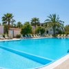 Una piscina all'aperto circondata da lettini e palme, con un cielo sereno.