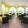 Un ristorante luminoso con tavoli apparecchiati, tende verde chiaro e finestre ampie.