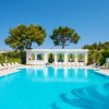 Piscina all'aperto con lettini bianchi e palme intorno, cielo blu.