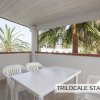 Terrazza coperta con tavolo bianco e sedie di plastica, vista su palme.