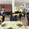 Una sala da pranzo spaziosa con tavoli apparecchiati e sedie nere. Persone al bancone sullo sfondo.