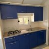 Cucina con mobili blu, fornelli a gas, lavabo e piccola finestra.