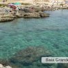 Acqua cristallina e rocce, persone godono il mare.