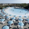 Persone in piscina circondata da ombrelloni azzurri.